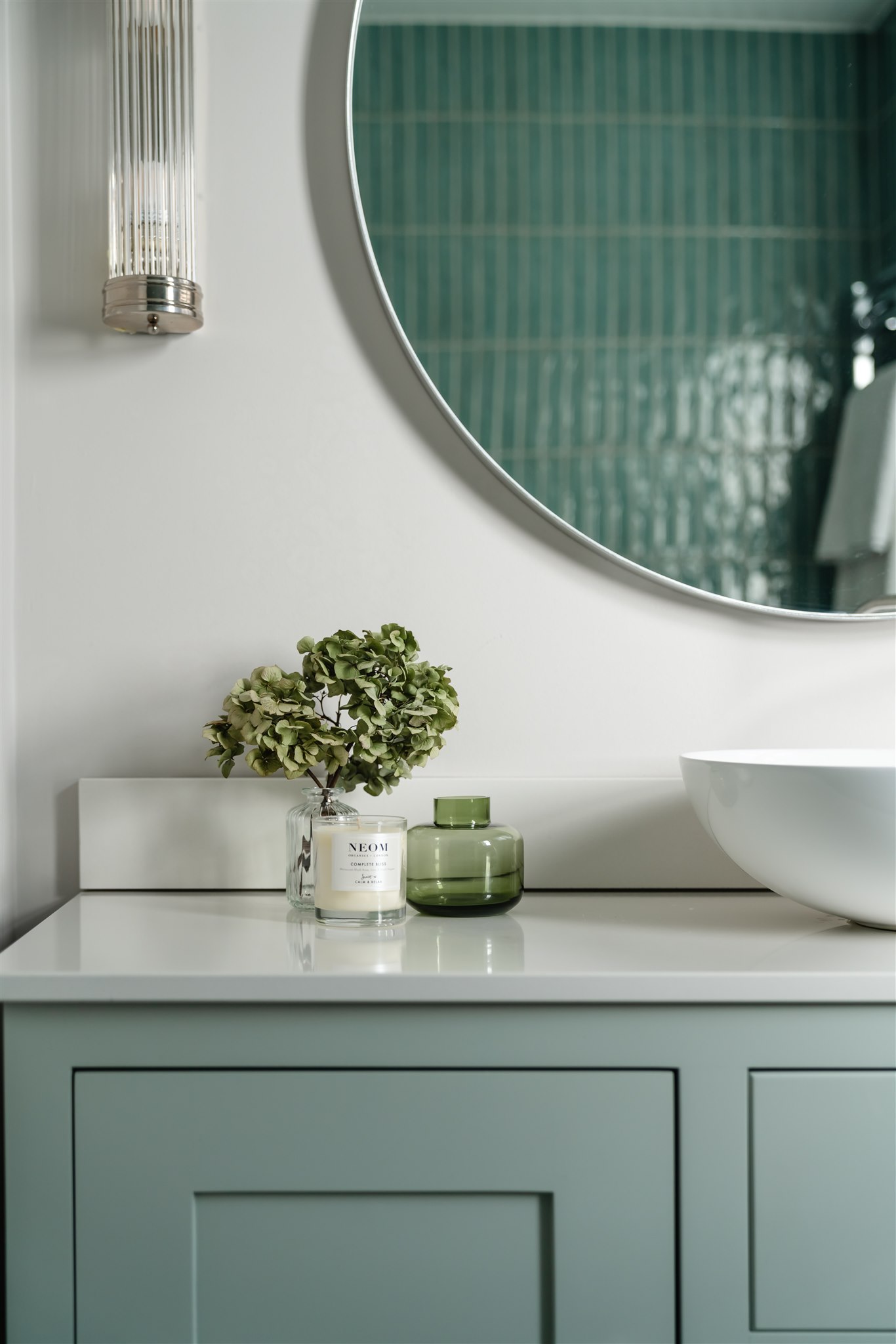 A bespoke shaker-style vanity unit in a soft duck egg blue, paired with a slimline worktop and vessel basin. The curved detailing and fluted glass wall light add a subtle nod to the home’s period character.