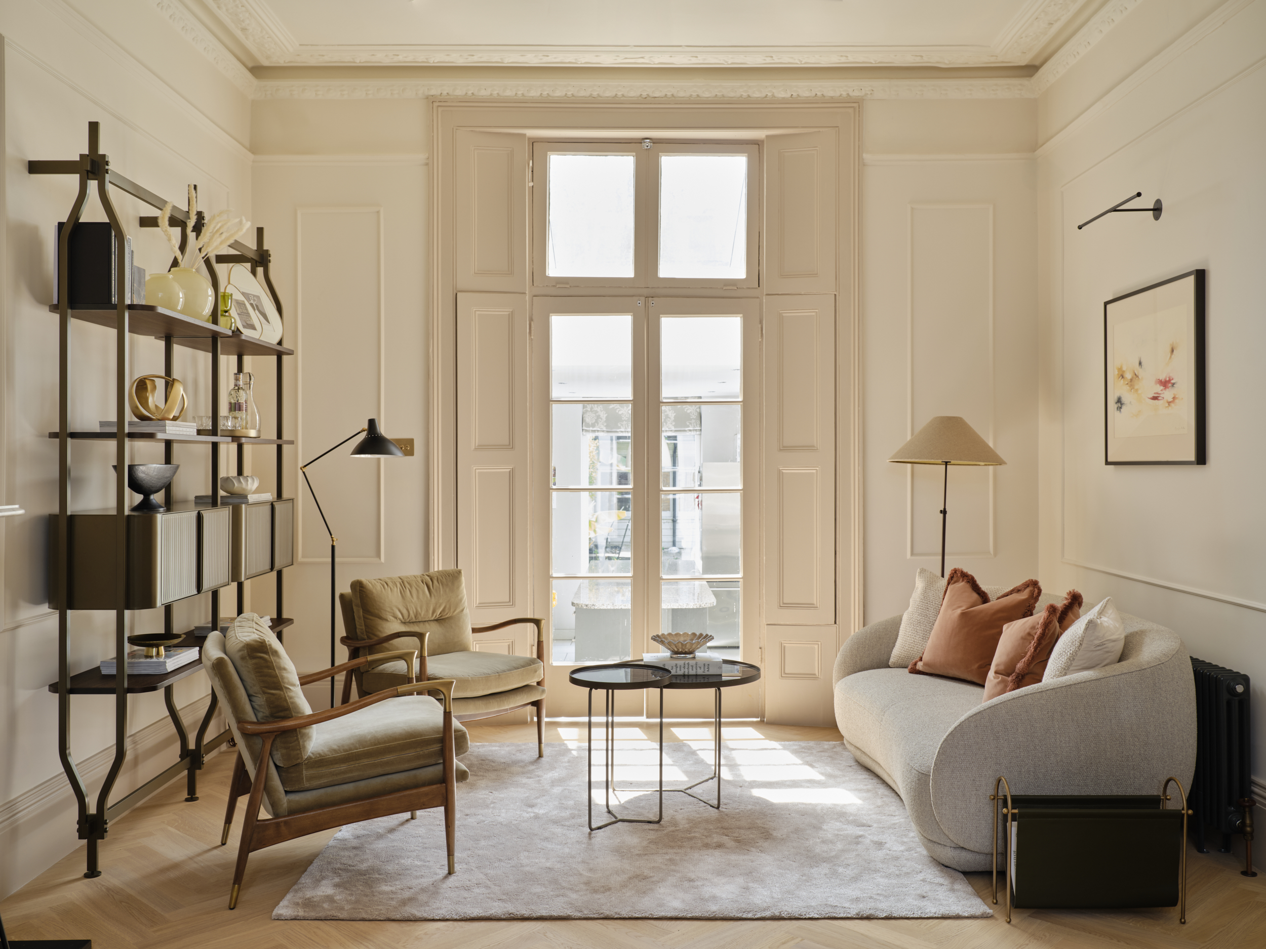 Layered lighting in a Victorian living room featuring a curved sofa, picture lights, tall sash windows and a sculptural floor lamp by Studio 3 Creatives