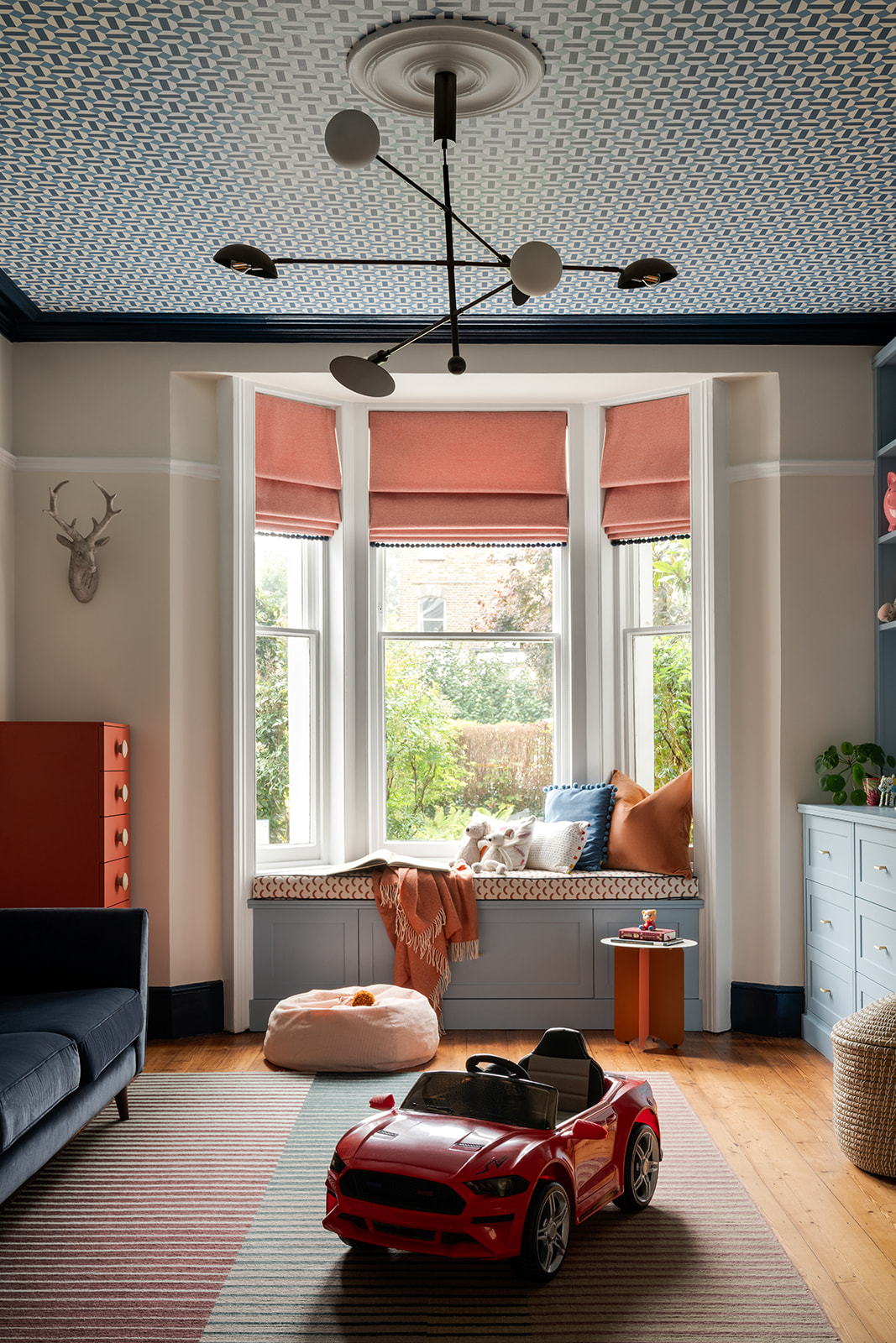 Victorian room with layered lighting featuring a modern chandelier, traditional ceiling rose, patterned wallpaper on the ceiling, and bold painted coving.