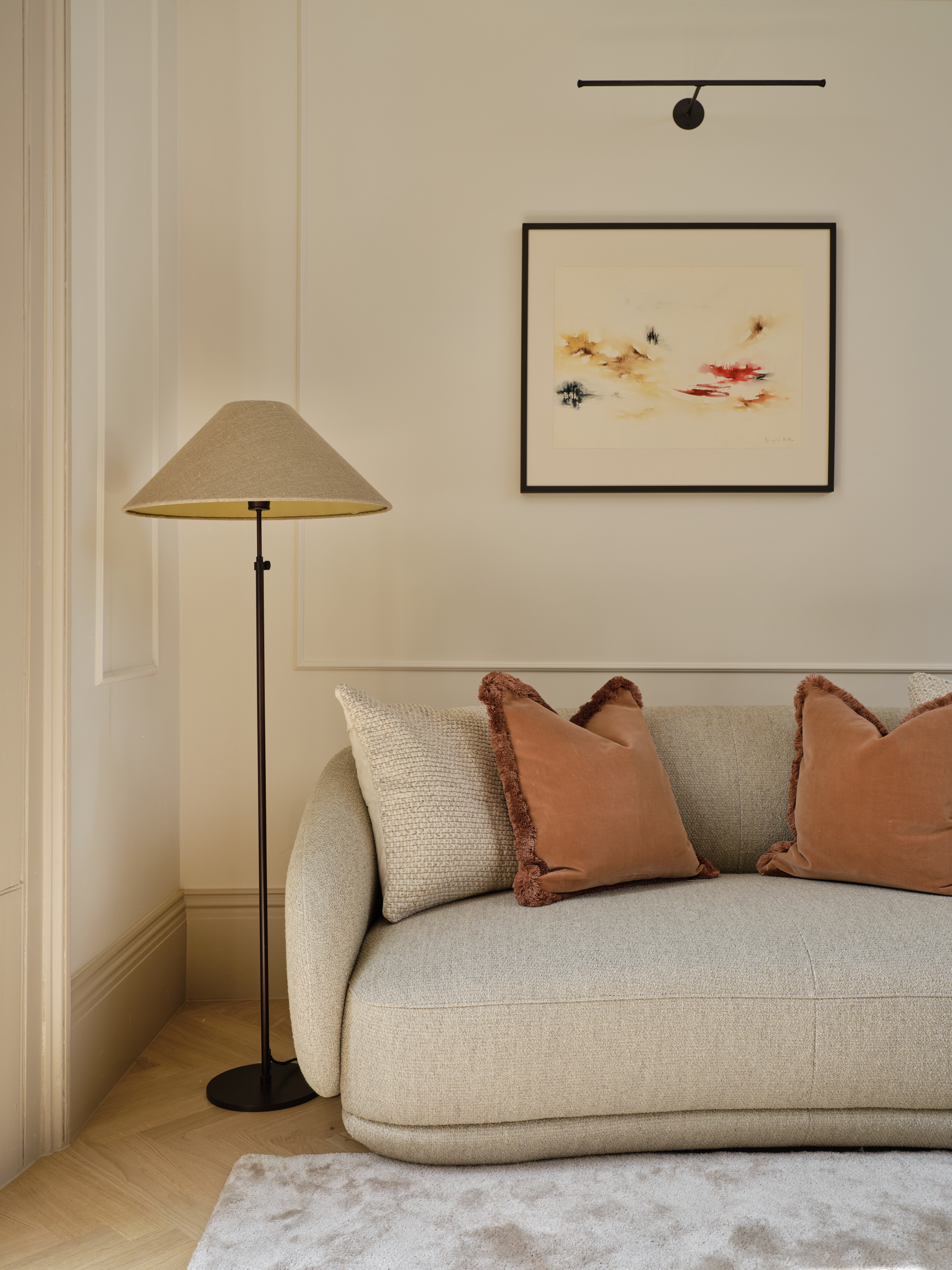 Detail of a living area with textured cushions, warm-toned floor lamp, and minimalist picture light, showcasing layered lighting in a period home.