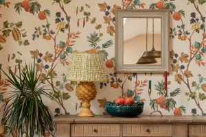 Botanical wallpapered London interior styled with a wooden dresser, ceramic lamp and mirror, showing affordable home styling and high-street design ideas.