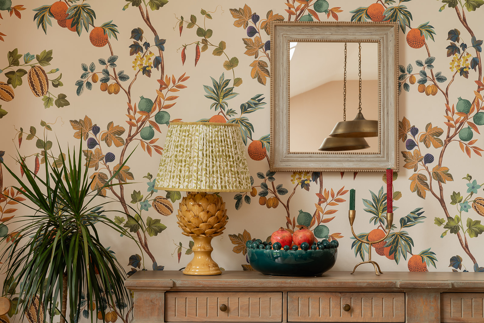 Botanical wallpapered London interior styled with a wooden dresser, ceramic lamp and mirror, showing affordable home styling and high-street design ideas.