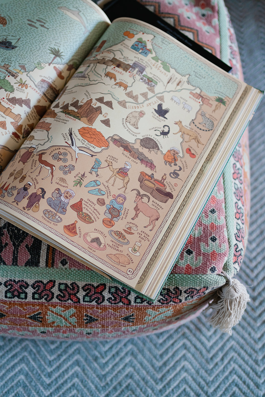 Illustrated travel book on a patterned pouffe, demonstrating affordable London home styling with meaningful, collected accessories