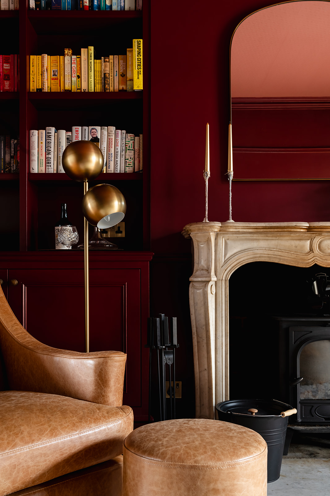 Burgundy library with leather armchair and marble fireplace, showing layered London interior design with characterful styling