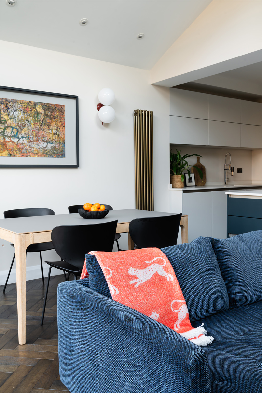 Modern dining and living space with navy sofa, brass radiator and layered textures in a Richmond home designed by Studio 3 Creatives.