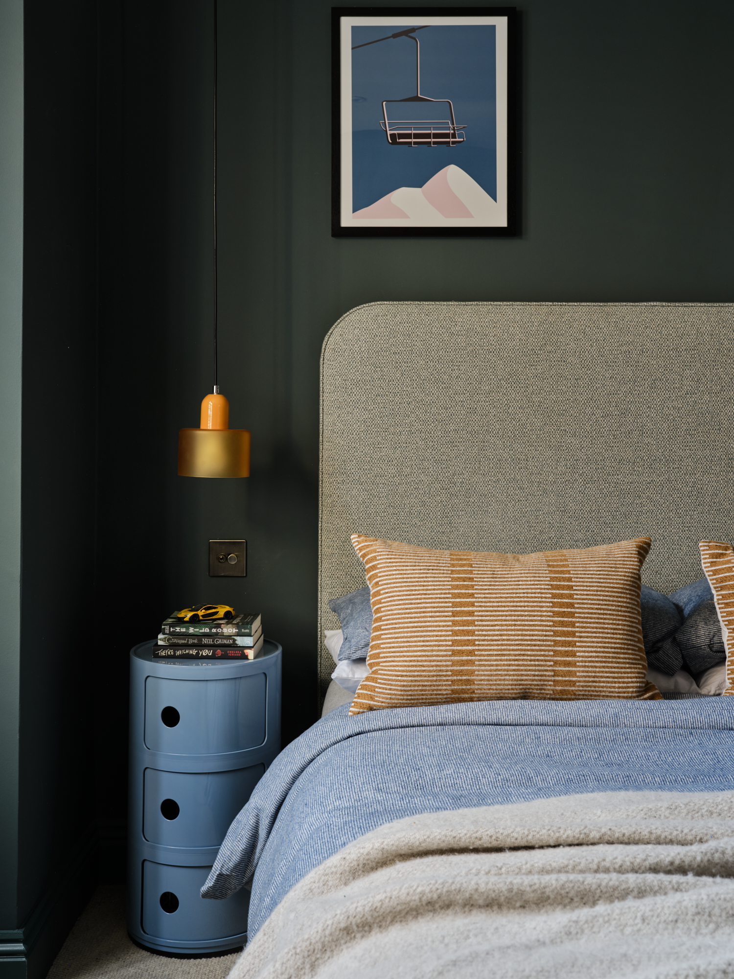 Forest green teenage bedroom bedside with amber pendant light, ski lift print and blue circular side table, interior design St Margarets London