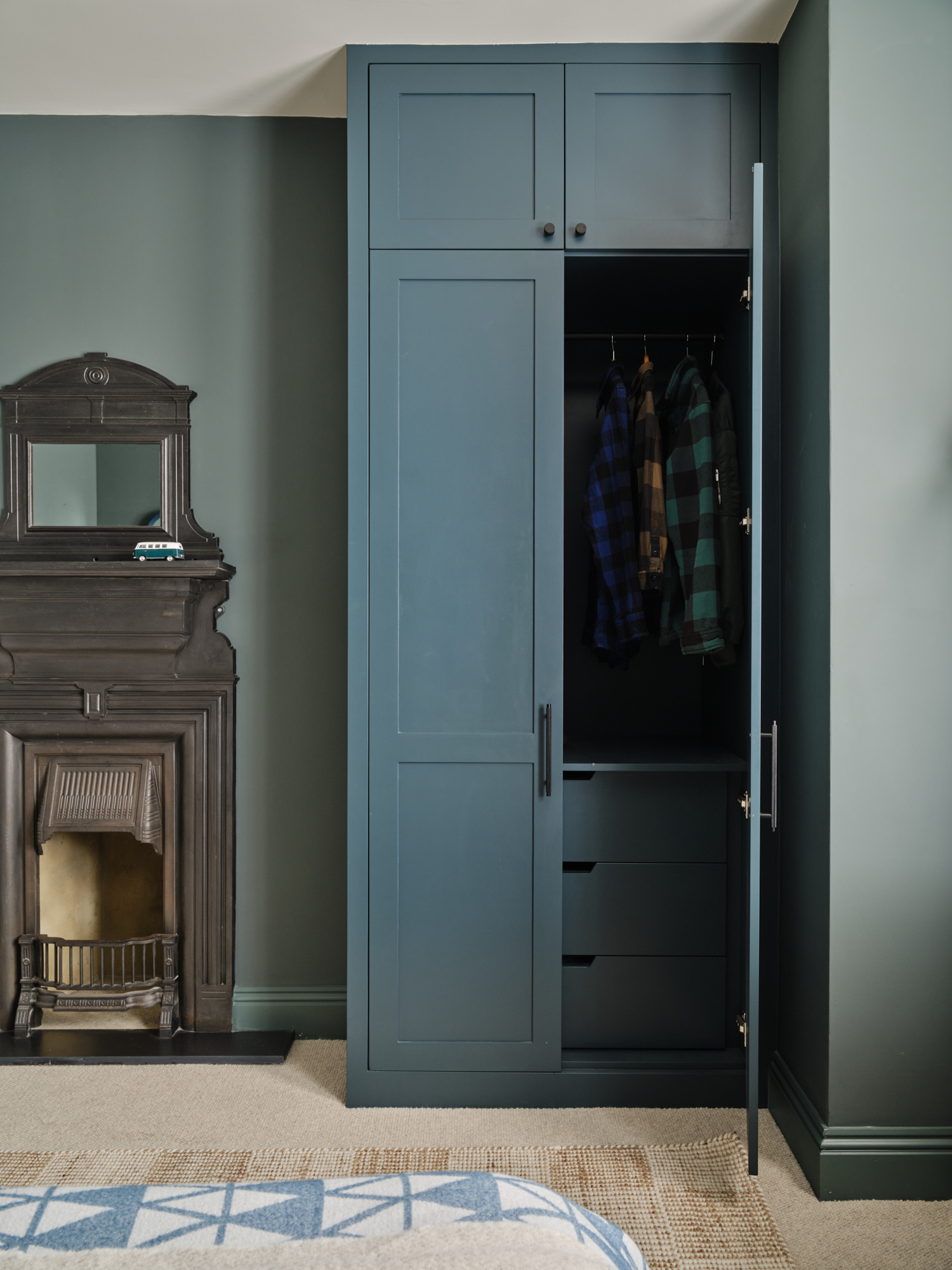 Teal fitted wardrobe open with clothes rail beside original Victorian cast iron fireplace, interior design St Margarets London