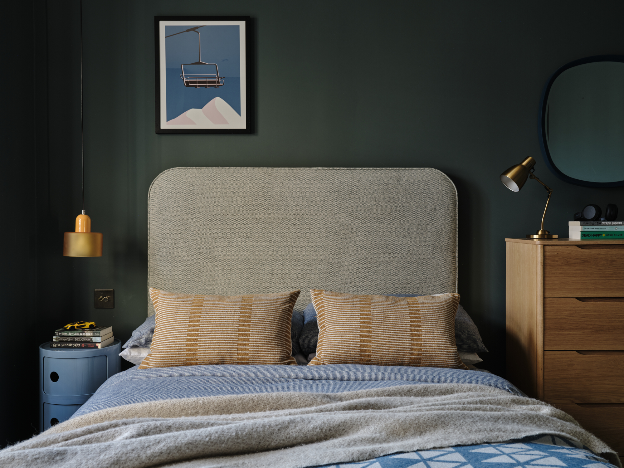 Forest green teenage bedroom with upholstered headboard, ski lift print, amber pendant and oak dresser with round mirror, London