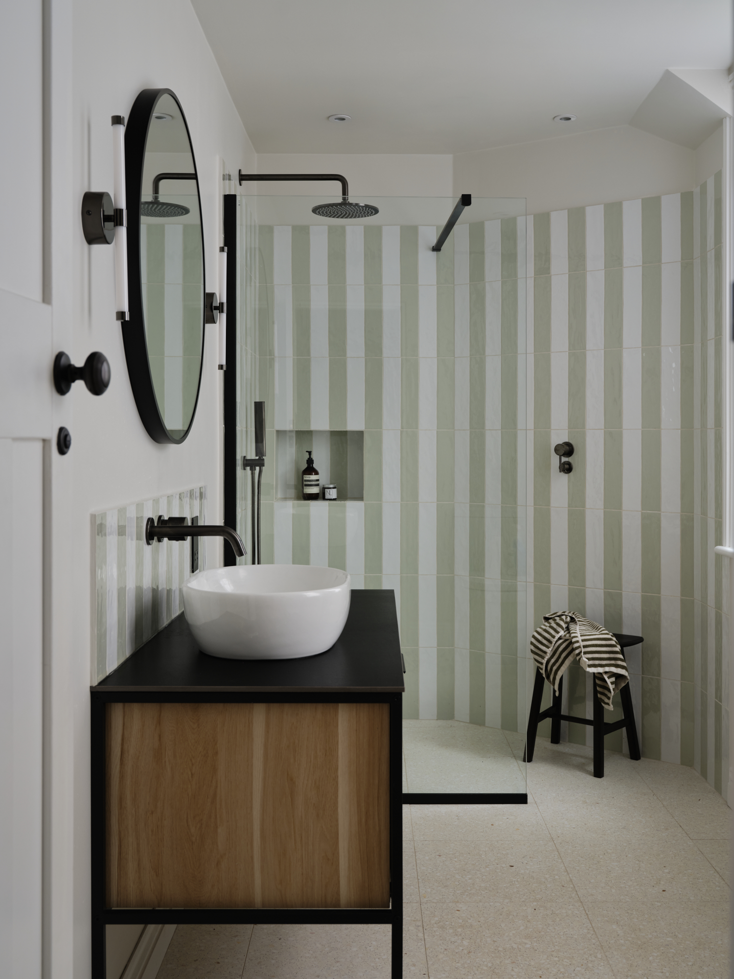 Sage green stripe tile bathroom with round mirror, vessel sink on black and oak vanity and walk-in shower, St Margarets London