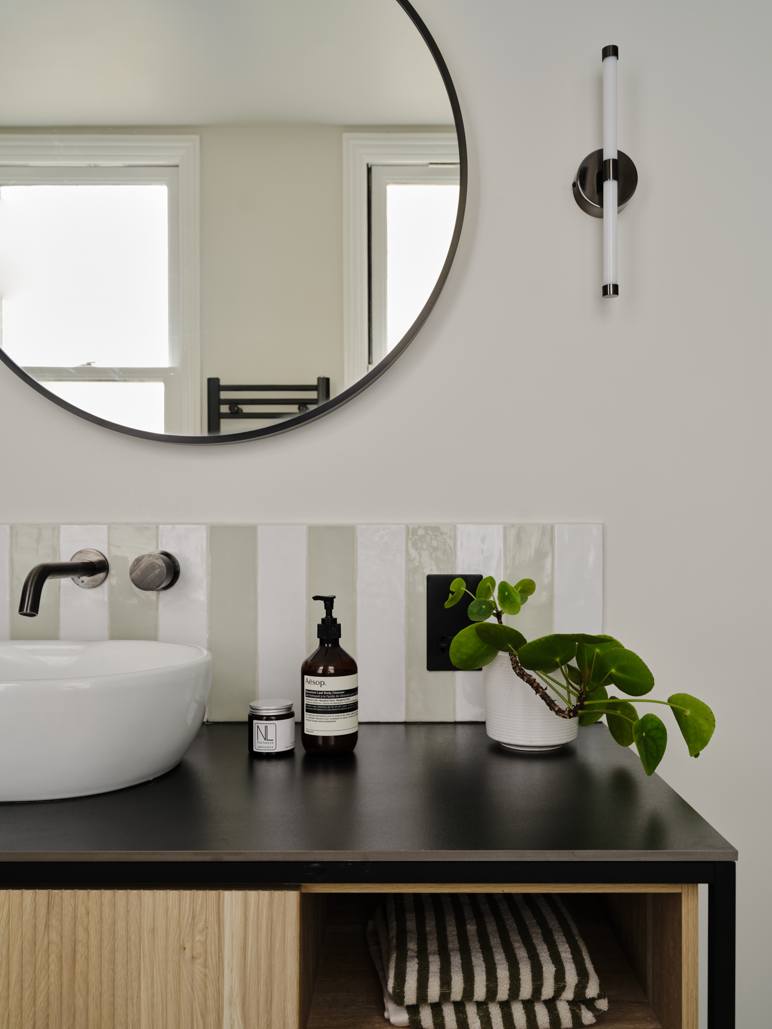 Bathroom vanity detail with round mirror, sage stripe tile backsplash, vessel sink and pilea plant, interior design St Margarets London