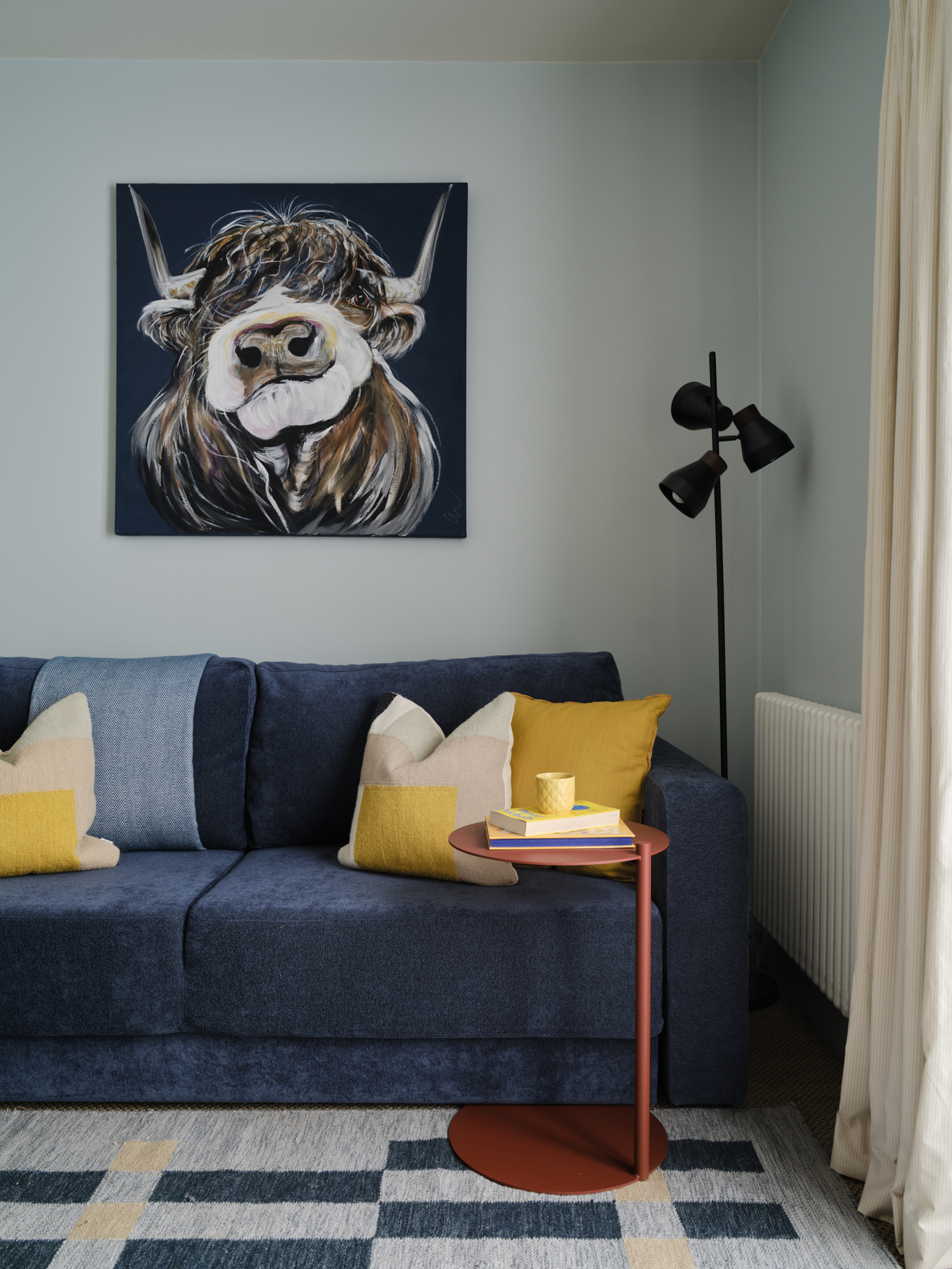 Dual-purpose snug with navy sofa, large highland cow canvas and yellow cushions, sage green walls St Margarets London