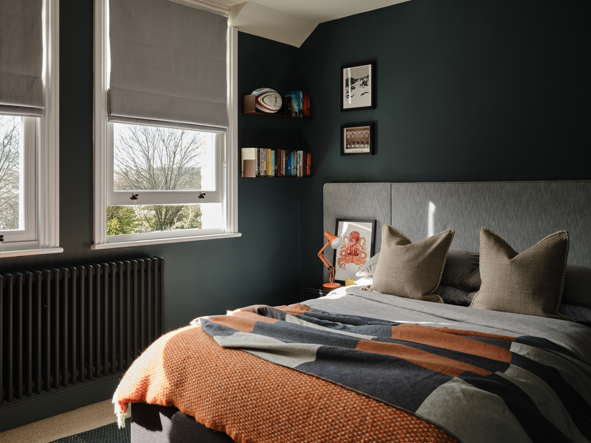 Forest green teenage bedroom with sash windows, roman blinds, corner bookshelves with rugby ball and orange Anglepoise lamp, London