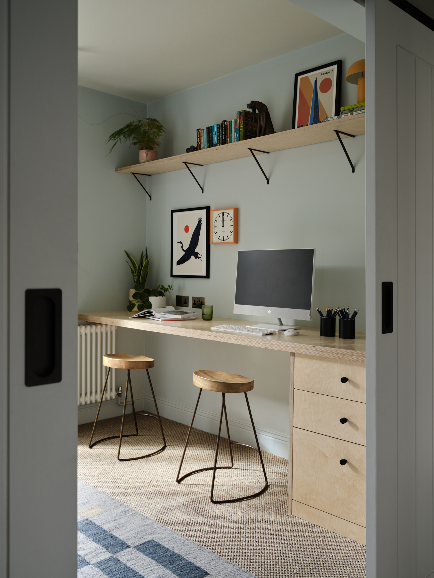 Bespoke home study with plywood desk and two stools viewed through sliding barn doors, interior design St Margarets London
